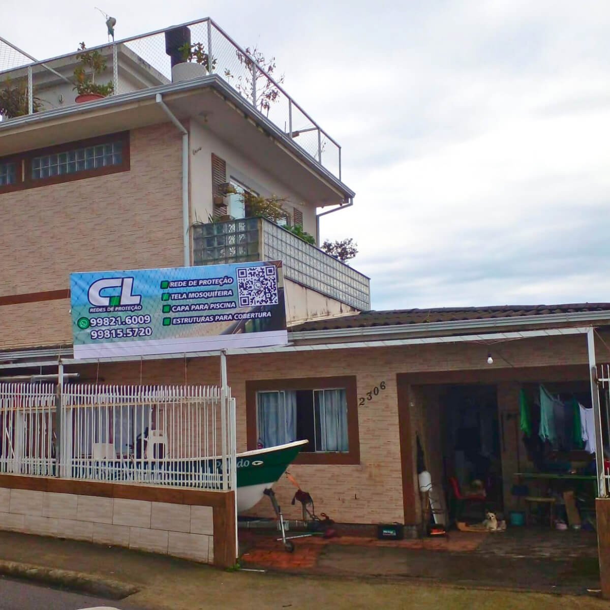 Fachada da sede da empresa exibindo um banner 'CL Redes de Proteção' fixado na grade superior e um barco estacionado na garagem aberta no térreo.