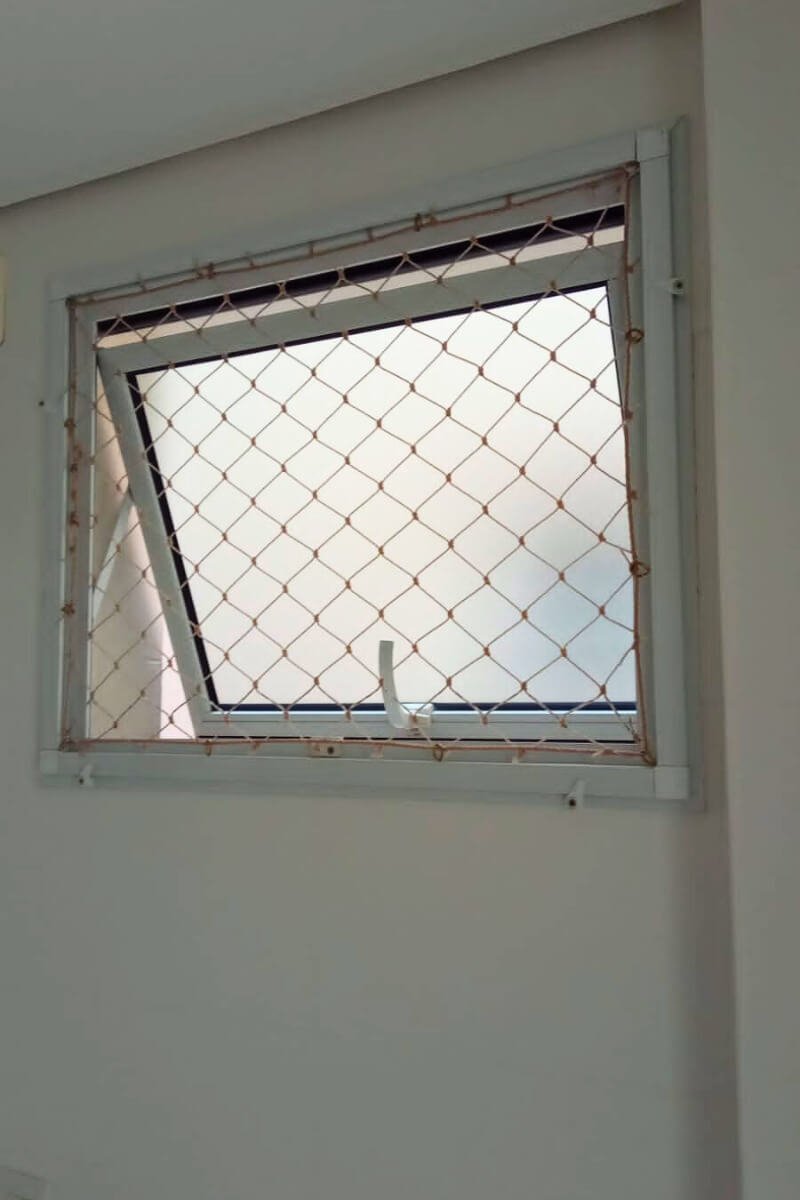 Janela tipo basculante (comum em banheiros e áreas de serviço) com vidro jateado, com a rede de proteção instalada na moldura interna.
