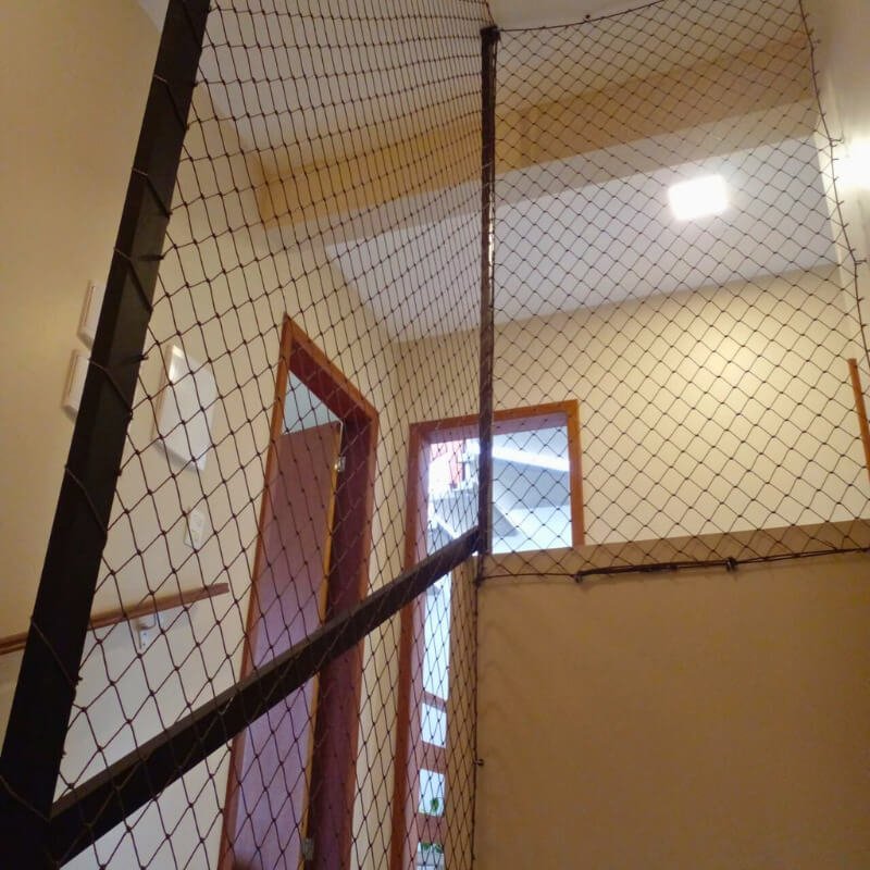 Instalação de rede de proteção preta na lateral de uma escada interna, garantindo segurança no corrimão e vão aberto.