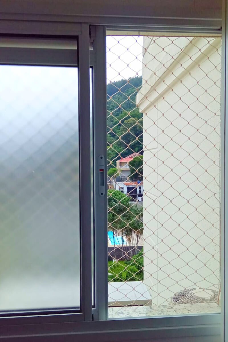 Criança segura próxima à janela com rede de proteção.