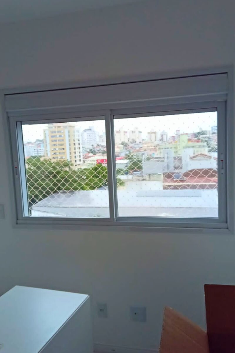 Janela com rede de proteção e vista urbana para telhados e casas na cidade.