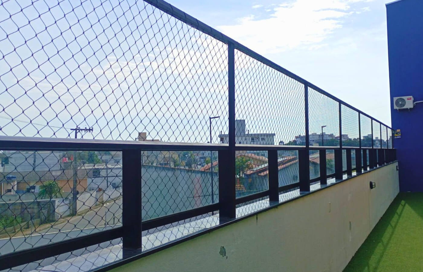 Estrutura metálica preta com rede de proteção instalada sobre mureta para segurança de área comum ou terraço.