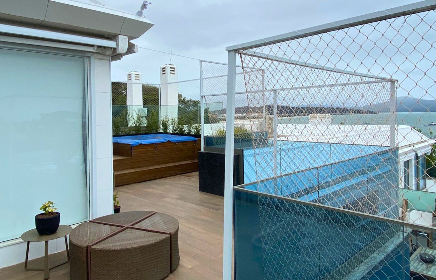 Terraço de cobertura com deck de madeira e jacuzzi, protegido por rede de segurança instalada em estrutura metálica branca.