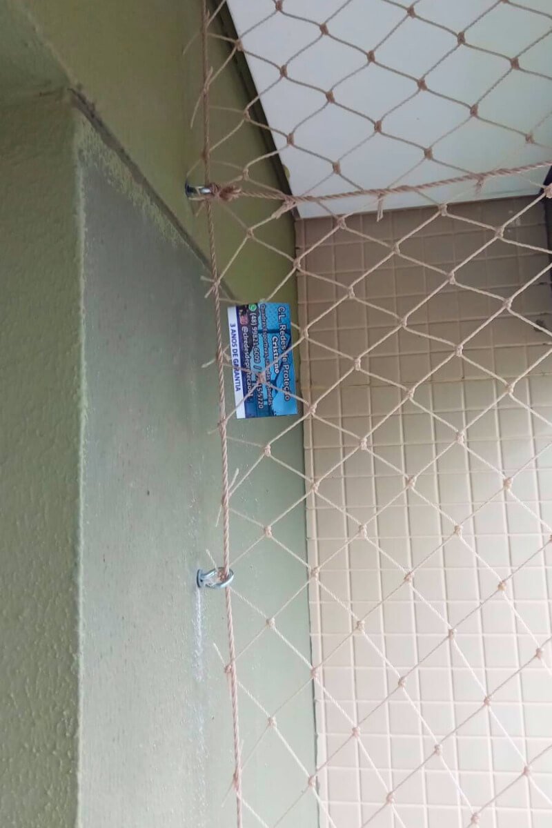 Detalhe aproximado da fixação de ganchos e cordas da rede de proteção em parede texturizada, garantindo alta resistência.