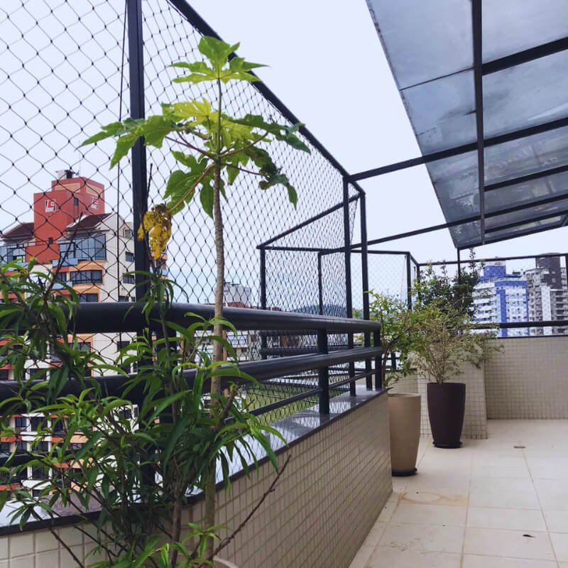 Área externa com plantas em vasos e estrutura metálica preta suportando a rede de proteção ao redor do terraço.